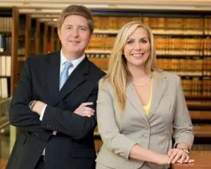 Portrait of a male lawyer and female lawyer dressed in suits, posing in front of rows of books.